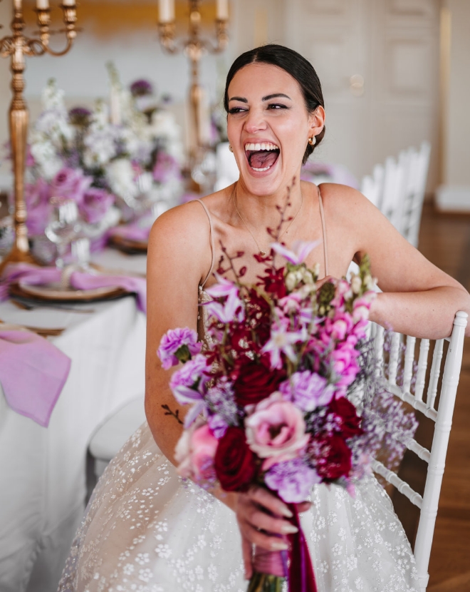 Hochzeitsfotograf in der Nähe: Lachende Braut mit farbenfrohem Hochzeitsstrauß am Tisch
